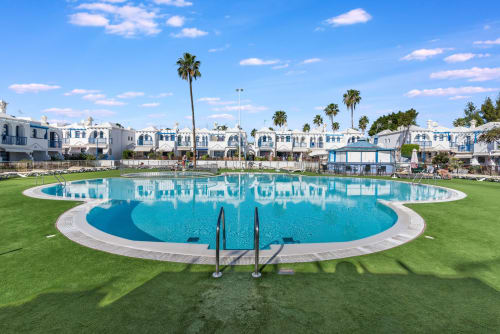 Gran piscina ovalada con agua turquesa rodeada de césped verde en el resort Home Stay Gran Canaria en Maspalomas, España
