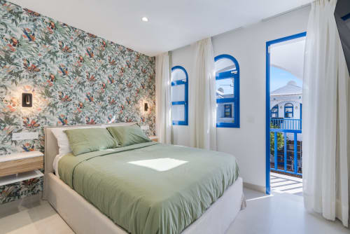 Dormitorio moderno en Flor del Almendro Bungalow en Maspalomas con papel tapiz floral, ropa de cama verde y vistas al mar azul desde el balcón