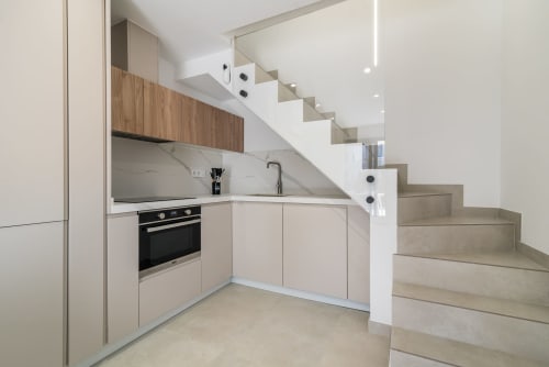 Cocina moderna con detalles en madera y backsplash de mármol bajo escaleras en bungalow Flor del Almendro, Maspalomas