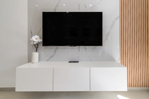 Sala moderna con TV montada en pared, muro de mármol blanco, unidad de entretenimiento minimalista y jarrón con flores blancas