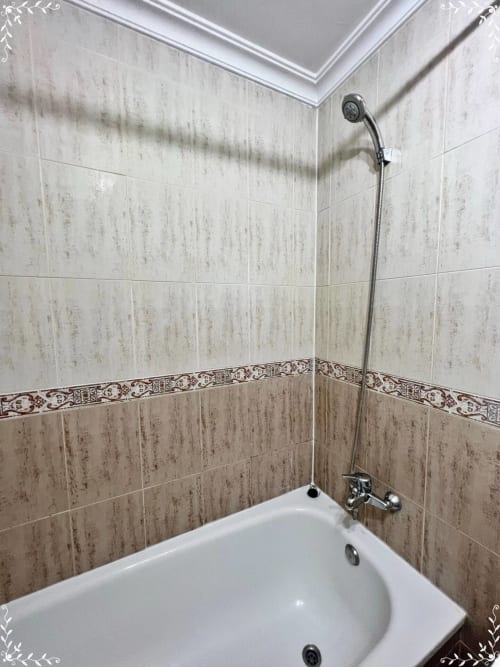 Baño con bañera blanca, paredes alicatadas con cenefa decorativa y alcachofa de ducha en apartamento de Fuengirola