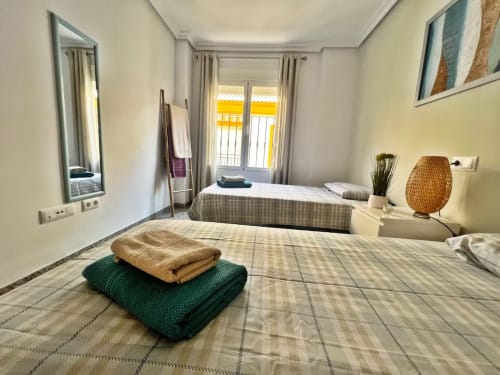 Luminoso dormitorio de apartamento frente al mar en Fuengirola con camas gemelas, toallas dobladas y vistas al mar a través de persianas amarillas