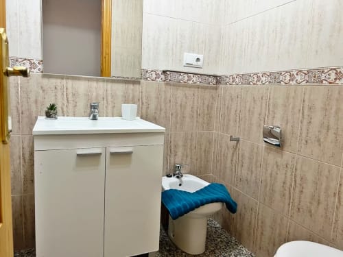 Baño moderno en apartamento de Fuengirola con lavamanos, bidé, paredes con azulejos de madera y cenefa decorativa