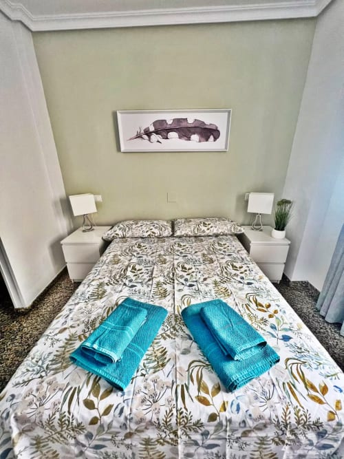 Dormitorio de apartamento frente al mar en Fuengirola con ropa de cama botánica, toallas azules y obra de arte de plumas