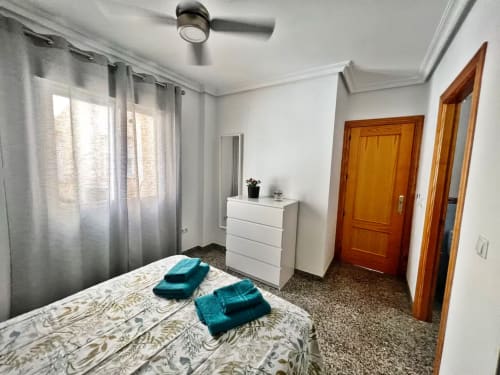 Dormitorio luminoso en Grupo Inmo House en Fuengirola con cama, cómoda blanca, puertas de madera y cortinas grises.