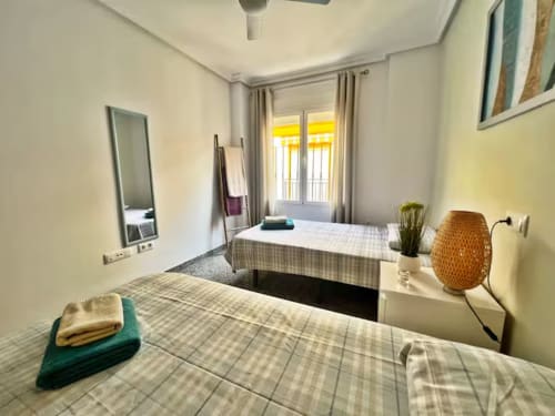 Moderno dormitorio doble con vistas al mar en apartamento de Fuengirola, con dos camas, espejo, puertas de balcón y decoración neutral