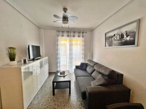 Moderno salón de apartamento en Fuengirola con sofá gris, televisor y acceso a balcón con vistas al mar