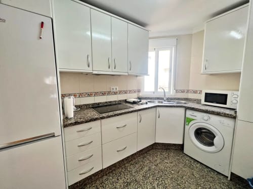 Cocina moderna blanca con encimeras de granito, lavadora y electrodomésticos de acero inoxidable en apartamento de Fuengirola
