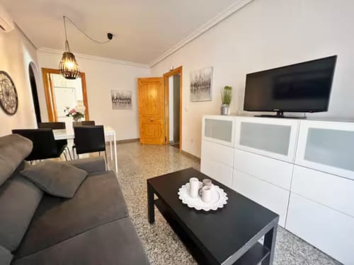 Moderno apartamento frente al mar en Fuengirola con sala de estar, TV pantalla plana, sofá oscuro y armarios blancos.