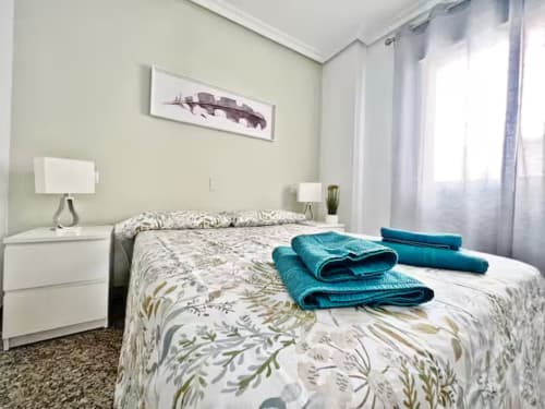 Dormitorio luminoso con ropa de cama floral, toallas turquesas y apartamento frente al mar en Fuengirola