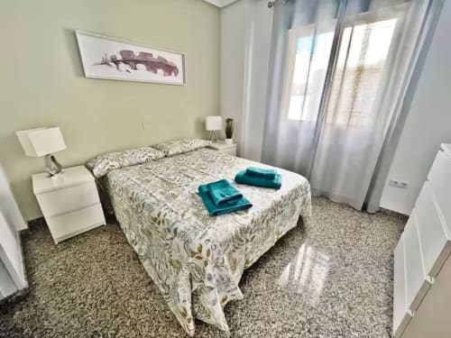 Dormitorio luminoso en apartamento frente al mar en Fuengirola con ropa de cama estampada, muebles blancos y luz natural del balcón