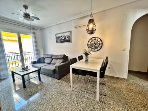 Moderno apartamento en Fuengirola con sofá gris, mesa de comedor, ventilador de techo, luminaria colgante y balcón con vista al mar