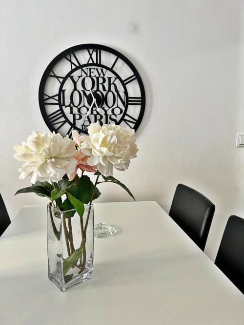 Elegantes peonías blancas en jarrón de cristal sobre mesa blanca con reloj decorativo de ciudades del mundo, decoración de apartamento en Fuengirola