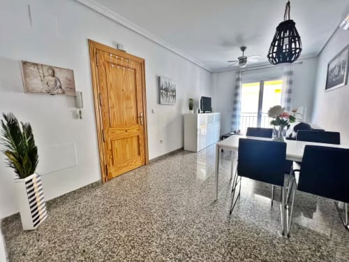 Sala de estar moderna en Fuengirola con mesa de comedor, maceta a rayas, puerta de madera y acceso a balcón con vistas al mar