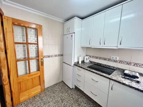 Cocina moderna con gabinetes blancos, encimeras de granito y puerta de madera en apartamento frente al mar en Fuengirola