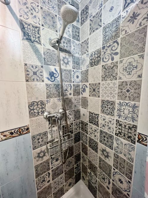 Cabina de ducha con azulejos decorativos en tonos azul y blanco, equipada con alcachofa de mano, en apartamento de Fuengirola