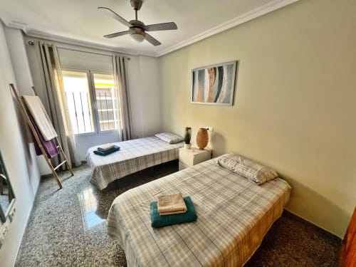 Dormitorio luminoso en apartamento de Fuengirola con dos camas, ventilador de techo, puertas al balcón y paredes amarillas