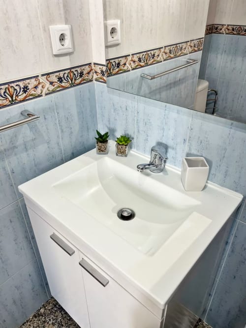 Moderno lavabo con vanidad blanca, paredes azuleadas en azul y cenefa decorativa en apartamento de Fuengirola