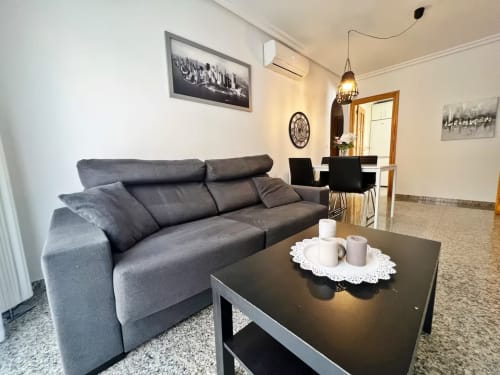 Moderno salón en Fuengirola con sofá gris, mesa de café negra y comedor con vistas al mar