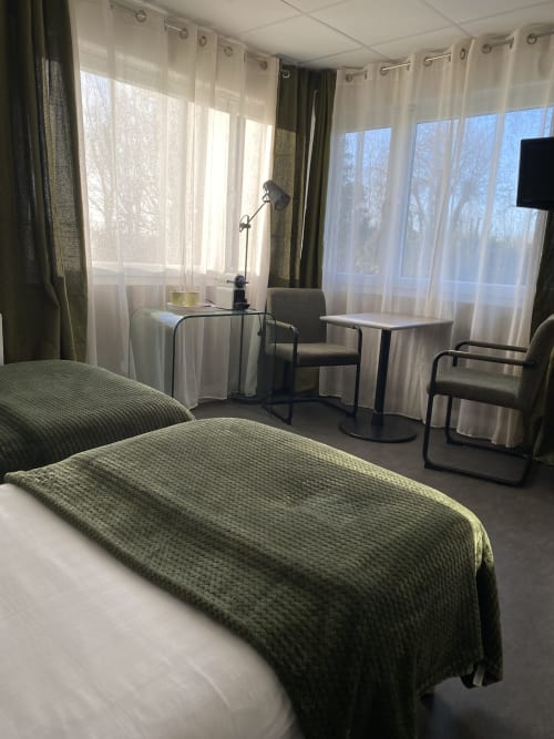 Chambre twin studio à l'hôtel Cosyade à Bourbourg avec lits jumeaux, bureau de travail, rideaux voilages et fenêtres avec vue sur le jardin