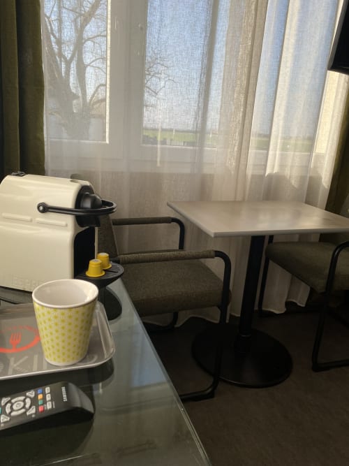 Kitchenette de studio avec cafetière, tasse jaune et table à manger avec vue sur le jardin à l'hôtel Cosyade à Bourbourg