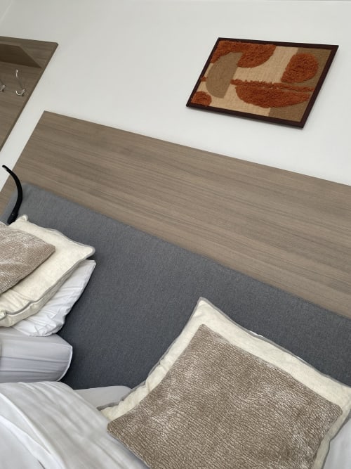 Chambre studio avec lit double gris tapissé, tête de lit en bois beige et art abstrait mural à Bourbourg