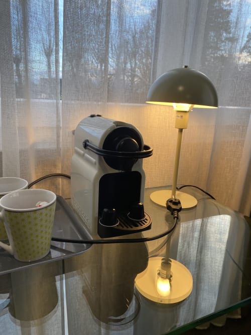 Studio cosy avec espace de travail, cafetière, lampe de bureau, tasses et vue sur le jardin à travers des rideaux voilages