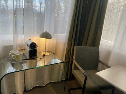 Espace de travail studio à l'hôtel Cosyade avec bureau en verre, cafetière, lampe de bureau et vue sur jardin