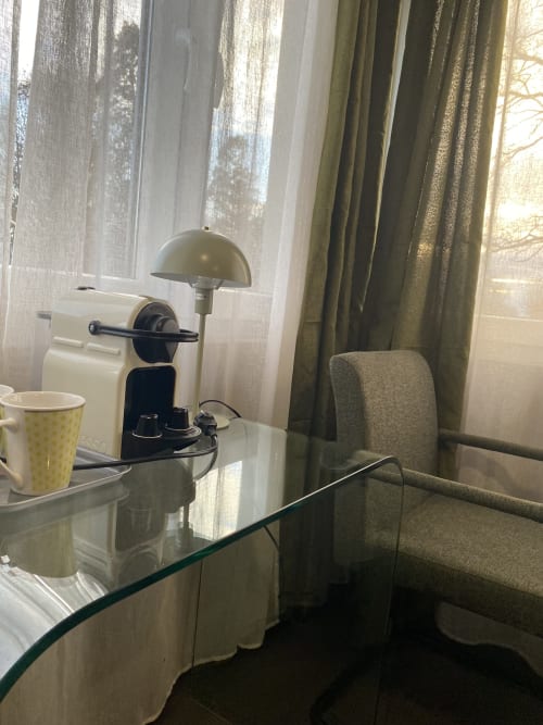 Espace de travail en studio à l'hôtel Cosyade avec bureau en verre, cafetière, lampe de bureau et vue sur le jardin