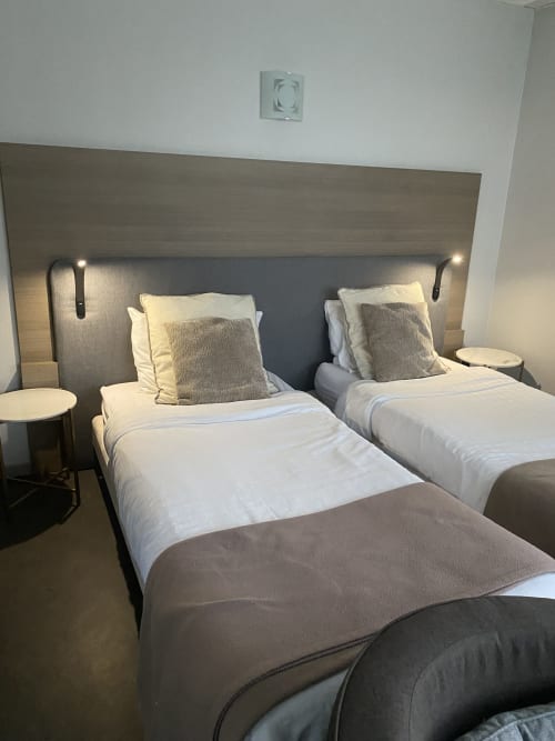 Lits jumeaux avec draps blancs et tête de lit grise dans un studio de l'hôtel Cosyade à Bourbourg, France