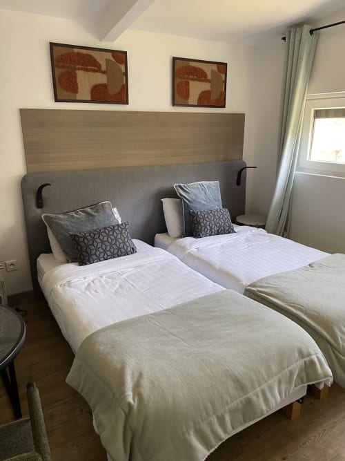 Chambre twin de l'hôtel Cosyade à Bourbourg avec draps blancs, tête de lit grise et oreillers décoratiifs