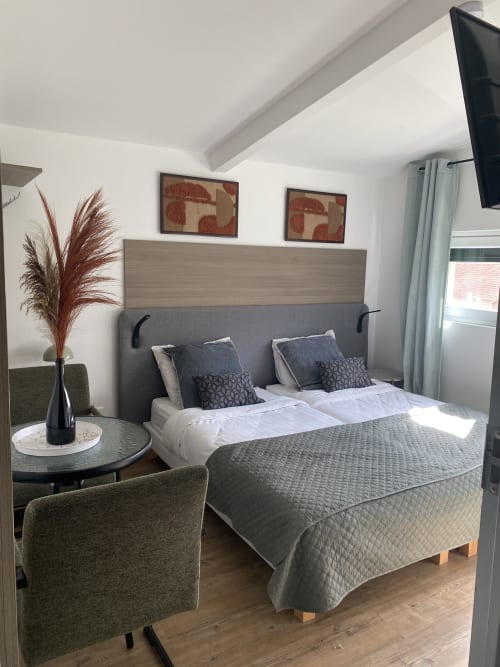 Chambre studio moderne à l'hôtel Cosyade à Bourbourg avec lit queen, tête de lit grise et vue sur le jardin