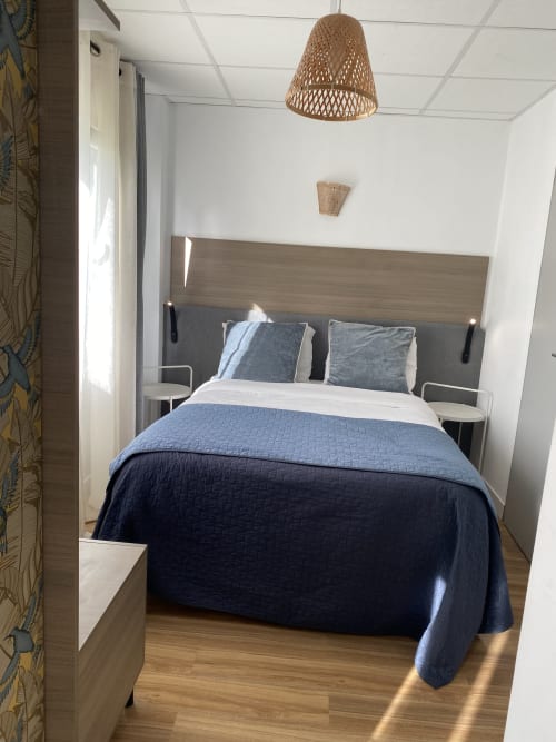 Chambre studio moderne à l'hôtel Cosyade à Bourbourg avec literie bleue, tête de lit en bois et luminaire suspendu tressé