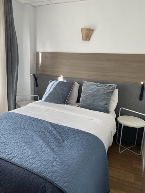 Chambre moderne de l'hôtel Cosyade à Bourbourg avec couvre-lit matelassé bleu, tête de lit capitonnée grise et vue sur le jardin