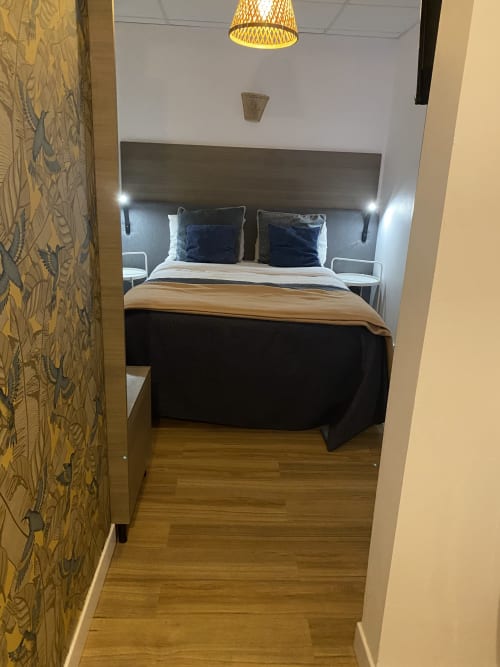 Chambre moderne à l'hôtel Cosyade à Bourbourg avec lit queen-size, tête de lit foncée, papier peint motifs et parquet