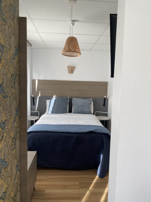 Chambre moderne du Cosyade hotel avec lampe suspendue tissée, tête de lit en bois, literie bleue et mur d'accent à motifs