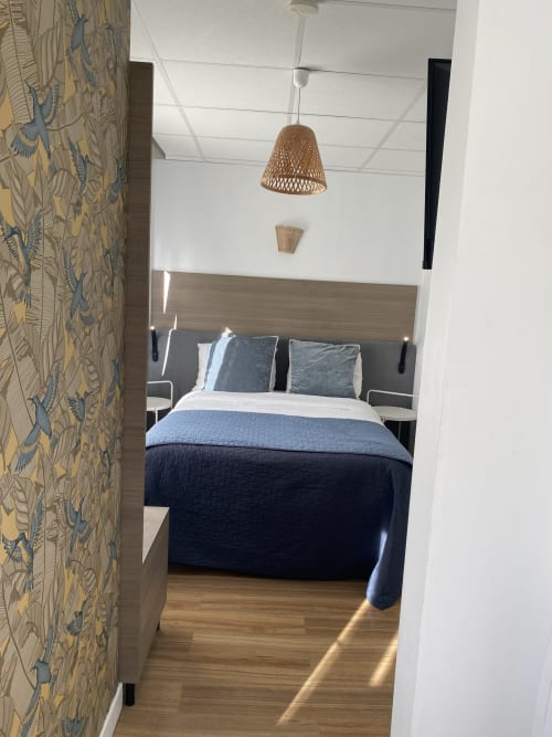 Chambre studio moderne à l'hôtel Cosyade à Bourbourg avec literie bleue, luminaire suspendu tressé et mur d'accent à motifs