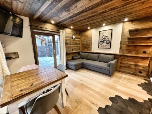 Modern wooden apartment interior at Chez Francine with gray sofa, dining table, kitchenette, and garden view in