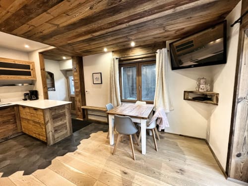 Modern apartment kitchen and dining area with wooden beams, white cabinetry, dining table, and garden views at Chez Francine,