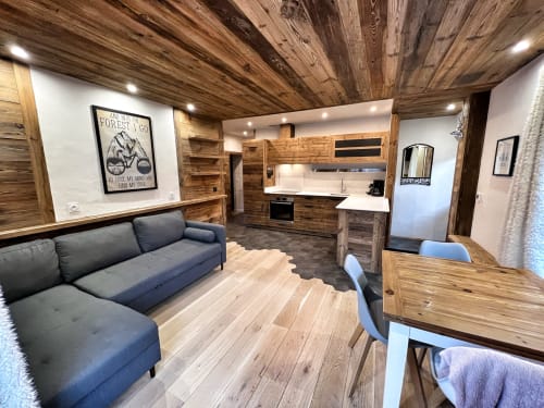 Modern apartment interior at Chez Francine with wooden ceiling, gray sofa, kitchen, and dining area in