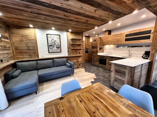 Modern alpine apartment with wood-paneled walls, blue sofa, dining table, and equipped kitchen in Chez Francine,