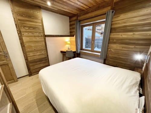 Modern bedroom in Chez Francine apartment with wooden beams, white bed, desk with lamp, and garden view in