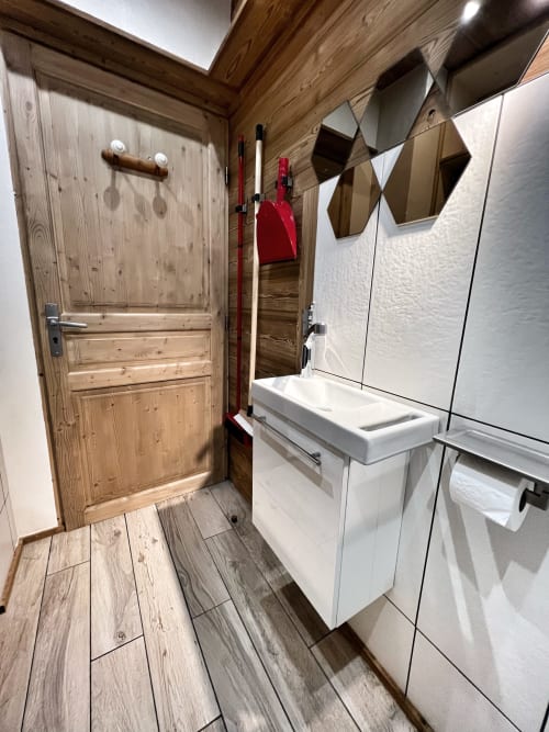 Modern bathroom in Chez Francine apartment with white sink, wooden door, and hexagonal mirrors in Notre-Dame-de-Bellecombe