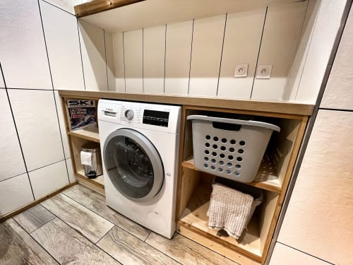 Modern laundry room with white washing machine and white laundry basket in wooden shelving at Chez Francine apartment,
