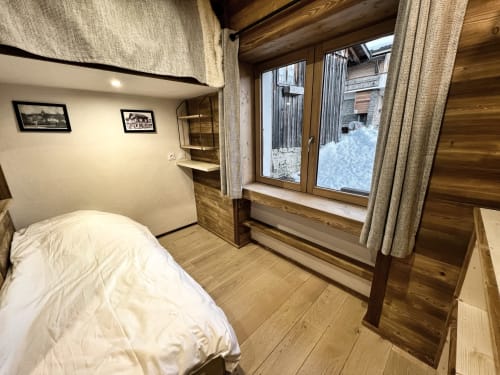 Cozy apartment bedroom at Chez Francine with wooden beams, white bed, and snowy garden view in Notre-Dame-de-Bellecombe