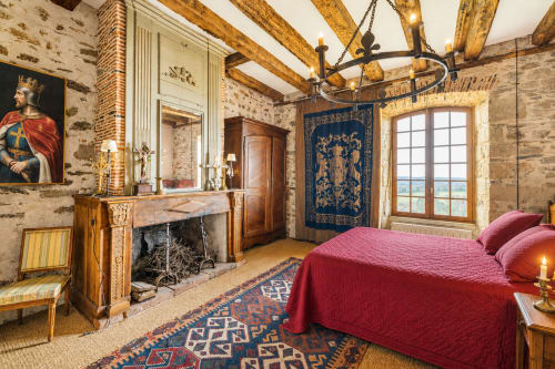 Chambre de style médiéval luxueuse au Domaine de Châlus-Chabrol avec poutres apparentes, cheminée, lit rouge et vue sur le jardin