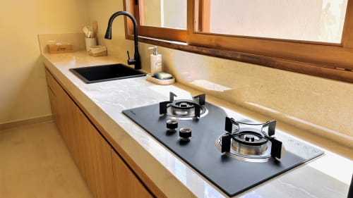 Modern kitchen in Oasis Dune Villas villa with black gas cooktop, black sink, marble countertop, and wooden cabinetry.
