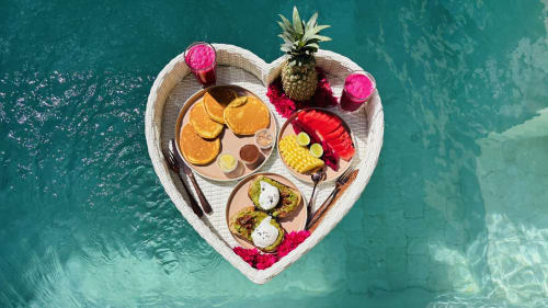 Aerial view of heart-shaped floating breakfast tray in turquoise pool at Oasis Dune Villas, Lombok, with tropical fruits and