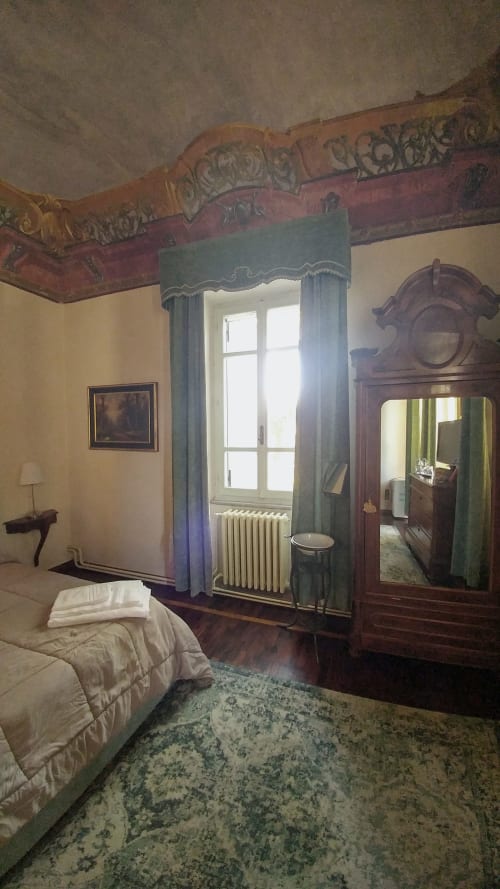 Historic bedroom at Bresbot B&B with ornate ceiling, wooden wardrobe, and garden view window in Bressana