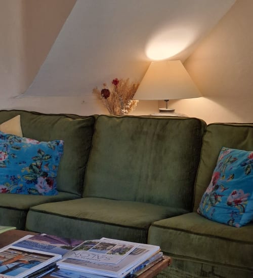 Chambre douillette en grenier au Mas des Vergers avec canapé vert, coussins fleuris, lampe et fleurs séchées à Salon-de-Provence